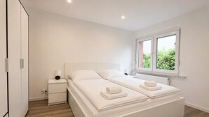 A modern bedroom with a large bed, bedside tables, a window with a view, and a wardrobe.