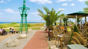 A beachfront restaurant with outdoor seating, a lighthouse, and a view of the ocean.