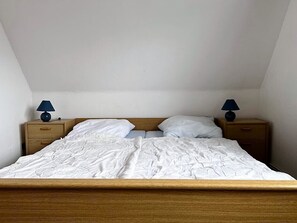 A bedroom with a wooden bed, white bedding, two bedside tables with lamps, and a sloped ceiling.