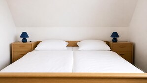 A double bed with a wooden headboard, two bedside tables with lamps, and a plain white wall.