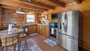 A wooden cabin kitchen with a large stainless steel refrigerator, wooden cabinets, and a dining table with chairs. - Beautiful log cabin w/ private dock, gameroom, 23mi to beach, 3bd2ba, sleeps 11 (Youngstown)