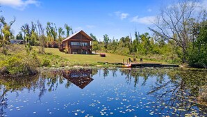 A lodge with a large deck and a dock extending into a pond with lily pads. - Beautiful log cabin w/ private dock, gameroom, 23mi to beach, 3bd2ba, sleeps 11 (Youngstown)