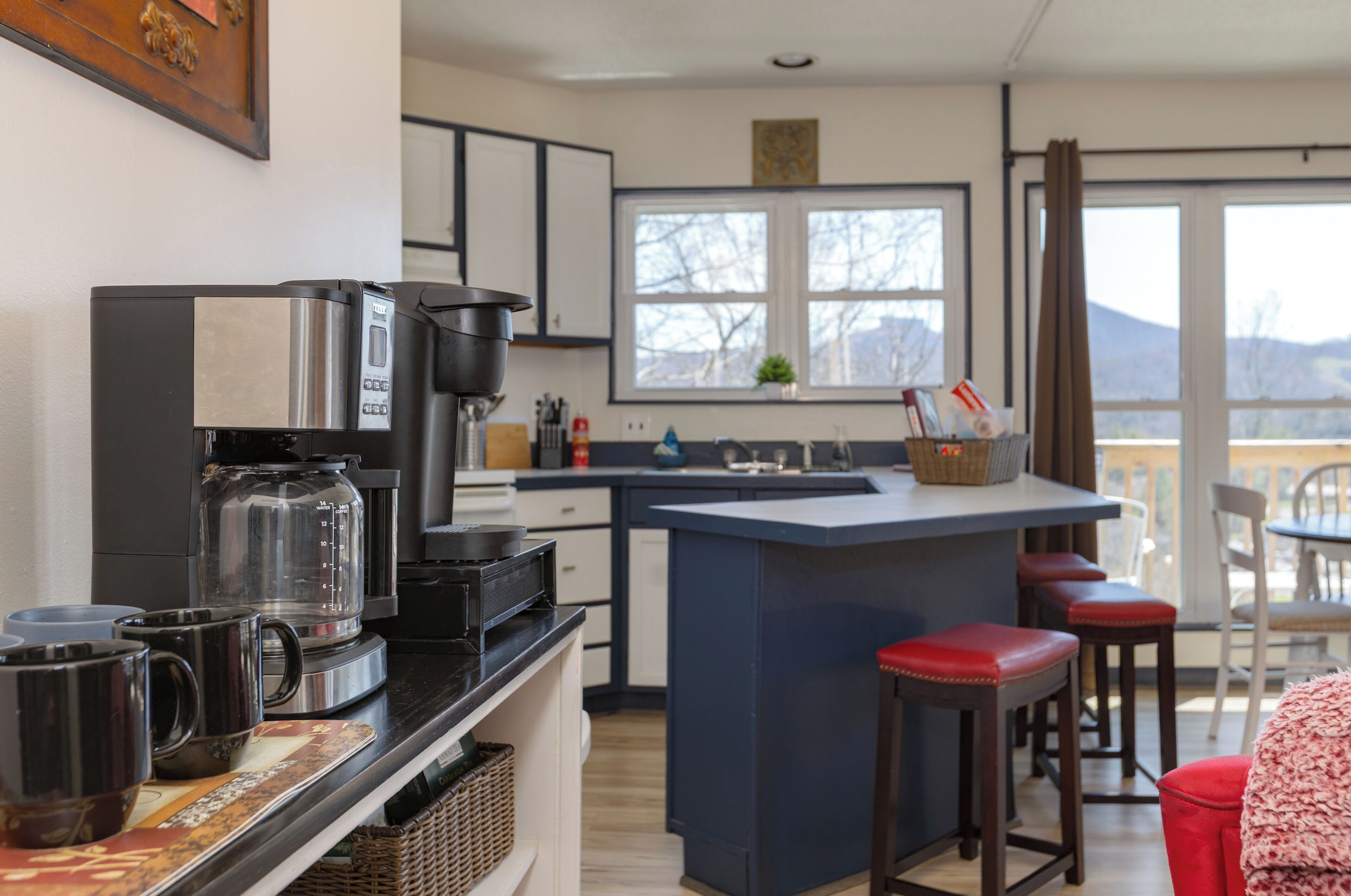 A modern kitchen with a coffee maker, a large window, and a bar area with stools.