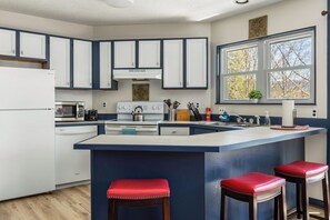 A kitchen with white cabinets, a central island with stools, a window with a view, and a microwave. - “Banner Elk Retreat -Walk to Town-Family-Friendly + A/C” (Banner Elk)