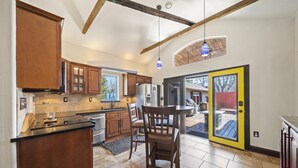 Una cocina con armarios de madera, encimera negra y una zona de comedor con mesa y sillas.