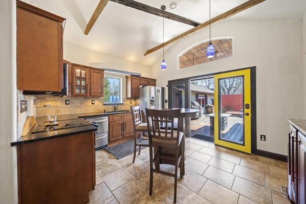 A kitchen with wooden cabinets, a black countertop, and a dining area with a table and chairs. - Gated Private Chalet with Hot Tub (Tulsa)