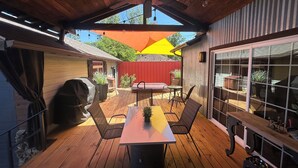 Un patio techado con una mesa y sillas, un ventilador de techo y vistas al jardín trasero.