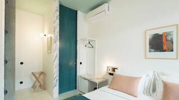 A hotel room with a bed, a nightstand, a hanging light, a framed artwork, and a shower area.