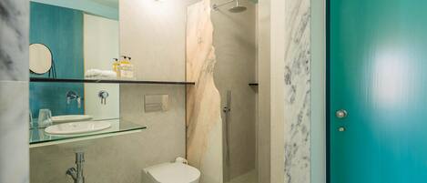 A bathroom with a glass sink, white toilet, and a shower with a marble wall.