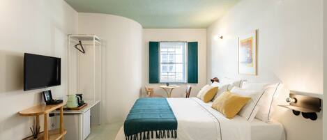 A bedroom with a bed, a TV, a desk, and a window.