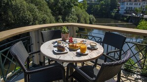 Ein runder Tisch mit Stühlen und einem Frühstücksaufstellplatz auf einem Balkon mit Blick auf einen Fluss.