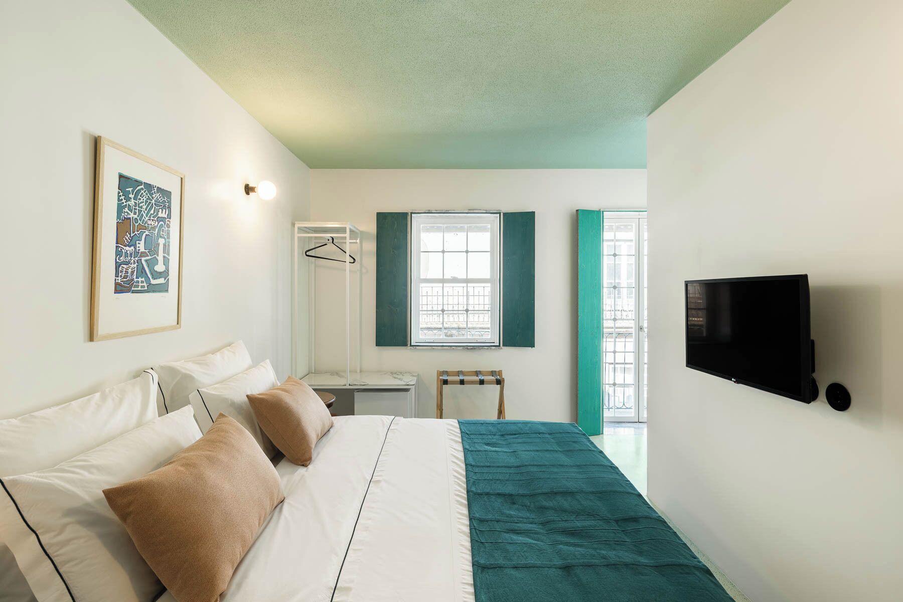 Ein Schlafzimmer mit Bett, Fernseher, Fenster mit Klappläden und einer Pendelleuchte.