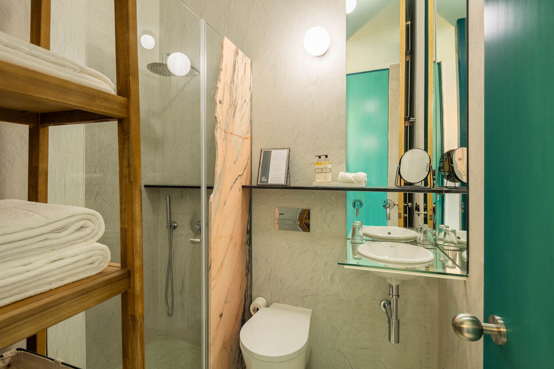 Een moderne badkamer met een glazen douchecabine, een toilet, een wastafel met een glazen plank en een spiegel met houten lijst.