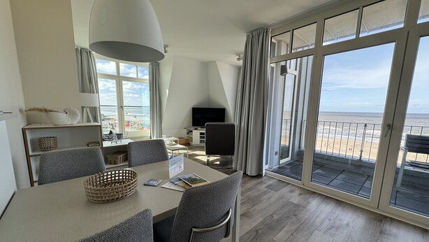A modern hotel room with a dining area, a flat-screen TV, and a large balcony with a view of the beach. - Anna Düne 3-44 - Exclusive sea view at Aparthotel Anna Düne (Wangerooge)