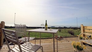 An outdoor patio with a table and chairs, overlooking a grassy area and the sea. - Stones throw from the sea (Seaford)
