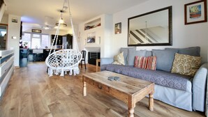 A spacious living area with a wooden coffee table, a grey sofa with patterned cushions, a white macrame chair, and a large mirror on the wall. - Stones throw from the sea (Seaford)