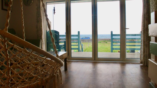 A room with a large sliding glass door leading to a deck with a view of the sea. - Stones throw from the sea (Seaford)