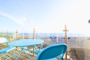 A balcony with a blue table and chairs, overlooking a beach with a parking area and a view of the ocean. - Serenity "your calm seafront retreat" (Seaford)