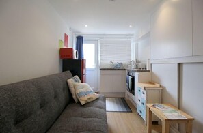 Un espacio habitable compacto con sofá, una mesita, kitchenette y ventana con persianas.