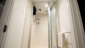 Ducha con cerramiento de vidrio, pared de azulejos blancos, ducha de mano y toallero con una toalla blanca.