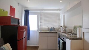 Una cocina compacta con refrigerador, horno, pileta y ventana con persianas.