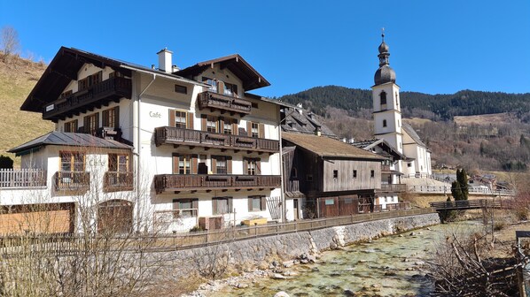 Una cabaña tradicional con un letrero de café, balcones de madera y una iglesia con campanario.