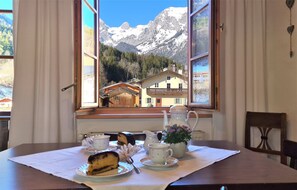 A table set with tea cups, a teapot, and a cake, with a mountain view through a window. - Sieger-Brandner Family Vacation Apartment in the mountaineering village of Ramsau (Ramsau)