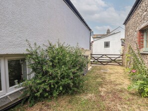 A narrow residential street with houses on either side, a wooden fence, and a small garden area with a bush. - Wrens Nest (Kingsbridge)