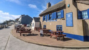 A traditional village pub with a signboard, outdoor seating, and a view of the sea. - Wrens Nest (Kingsbridge)