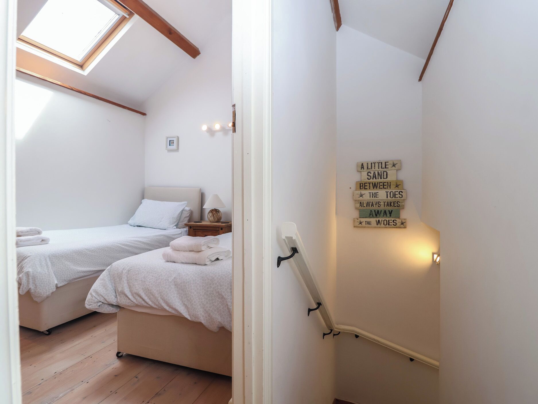 A bedroom with two beds, a bedside table, a lamp, and a wall-mounted sign.