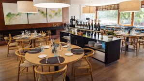 A restaurant interior with round wooden tables, chairs, and a bar area with wine bottles. - Hotel Xalet del Golf (Bolvir)
