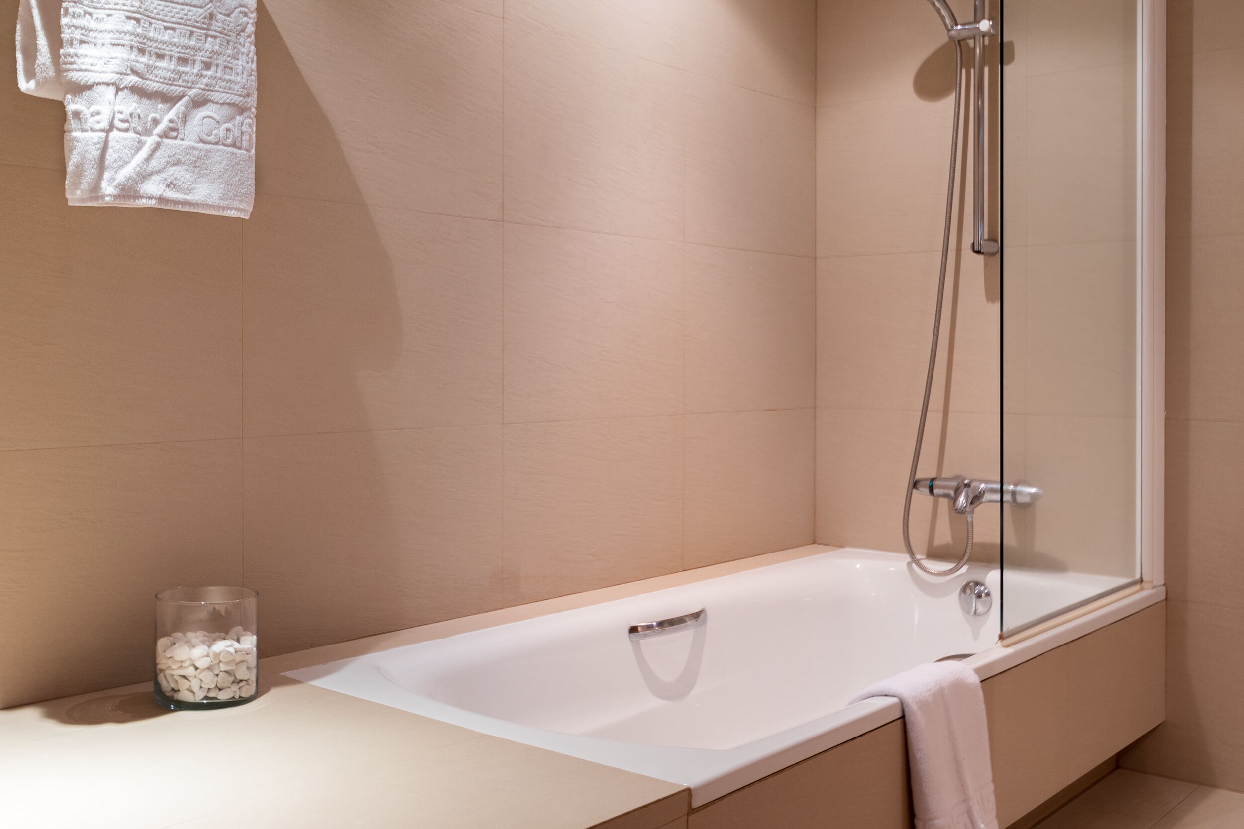 A modern bathroom with a bathtub, shower, and a glass container on the counter.