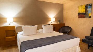 Habitación de hotel con una cama grande, dos lámparas de noche, una silla y un cuadro en la pared.