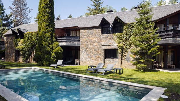 A modern building with a stone facade, a swimming pool, and outdoor seating. - Hotel Xalet del Golf (Bolvir)