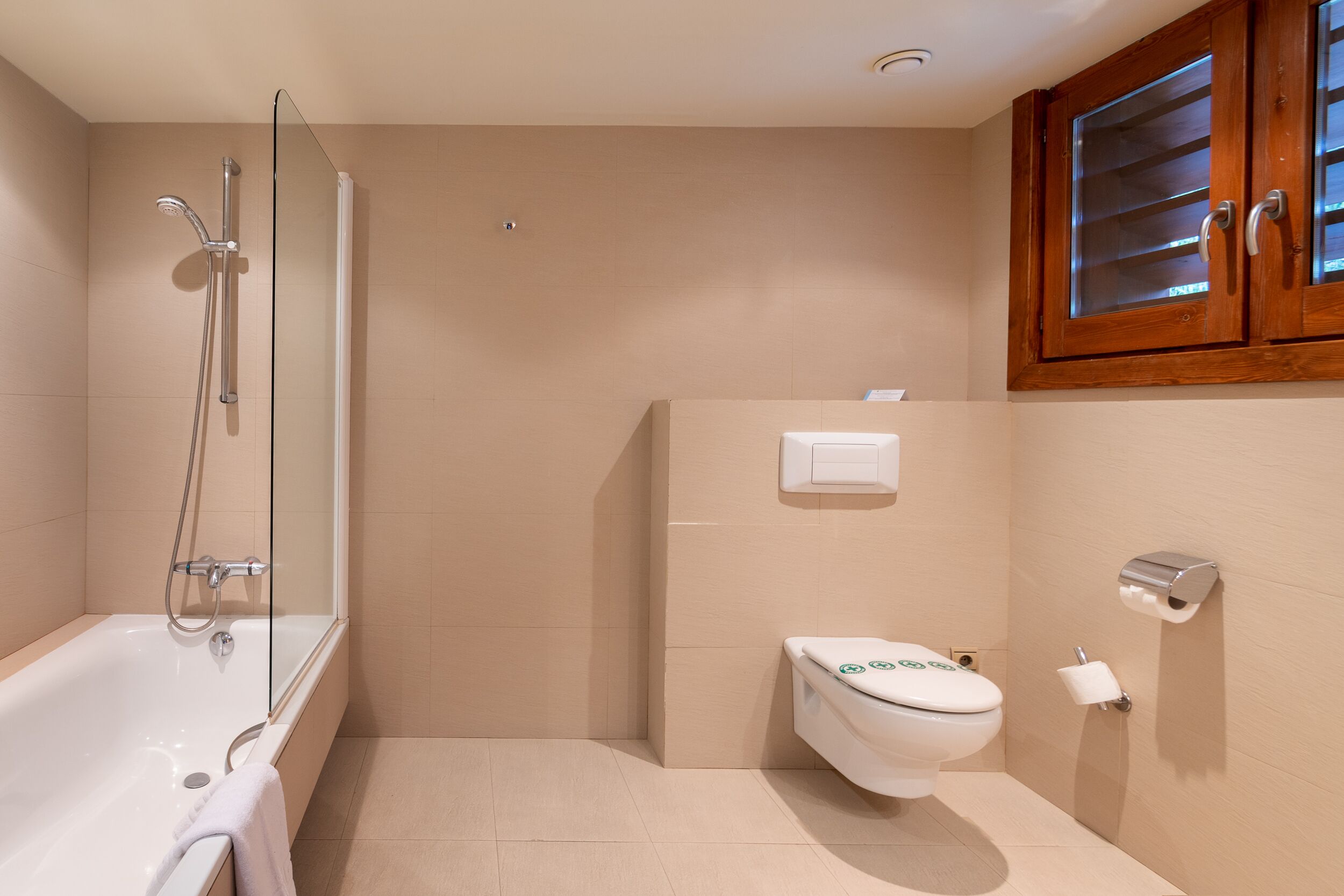 A modern bathroom with a bathtub, shower, toilet, and wooden cabinets.