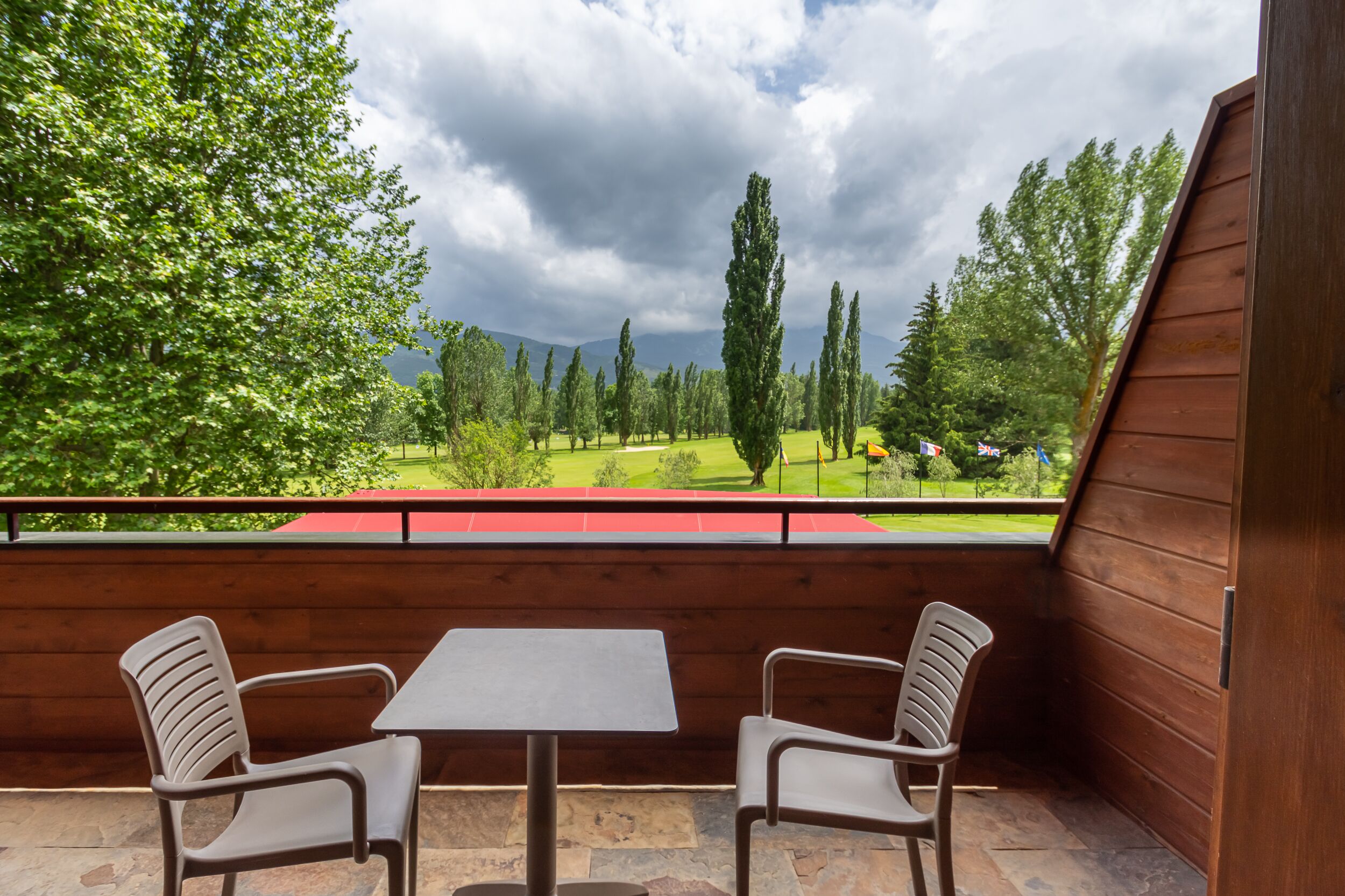 A balcony with two chairs and a table, overlooking a green landscape with trees and a golf course.