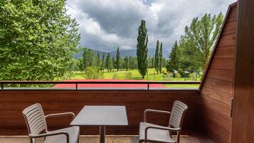 A balcony with two chairs and a table, overlooking a green landscape with trees and a golf course.