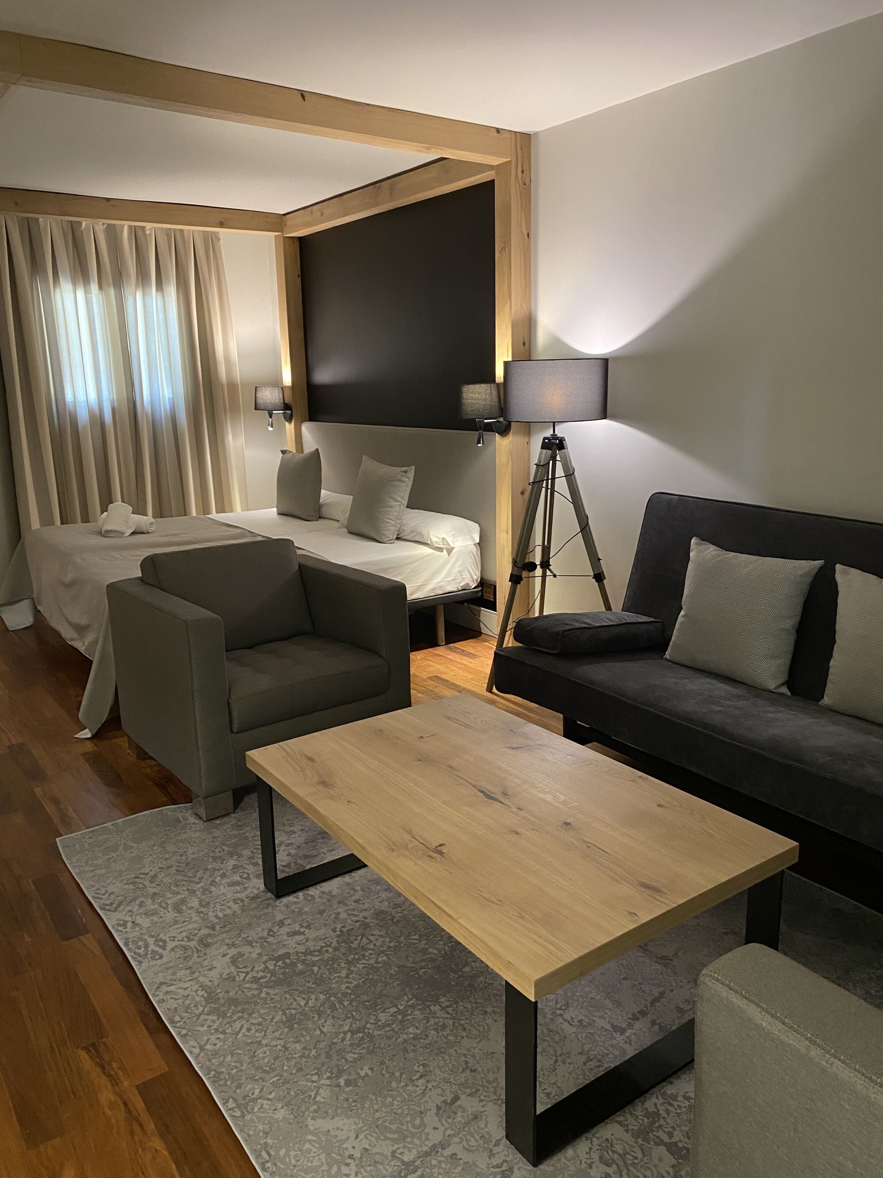 A modern hotel room with a bed, two sofas, a coffee table, and a desk lamp.