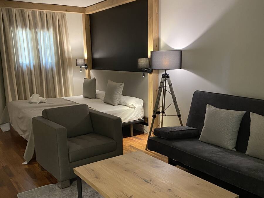 A modern hotel room with a bed, two sofas, a coffee table, and a desk lamp.