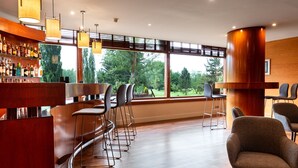 A bar area with wooden flooring, bar stools, and a large window offering a view of trees. - Hotel Xalet del Golf (Bolvir)