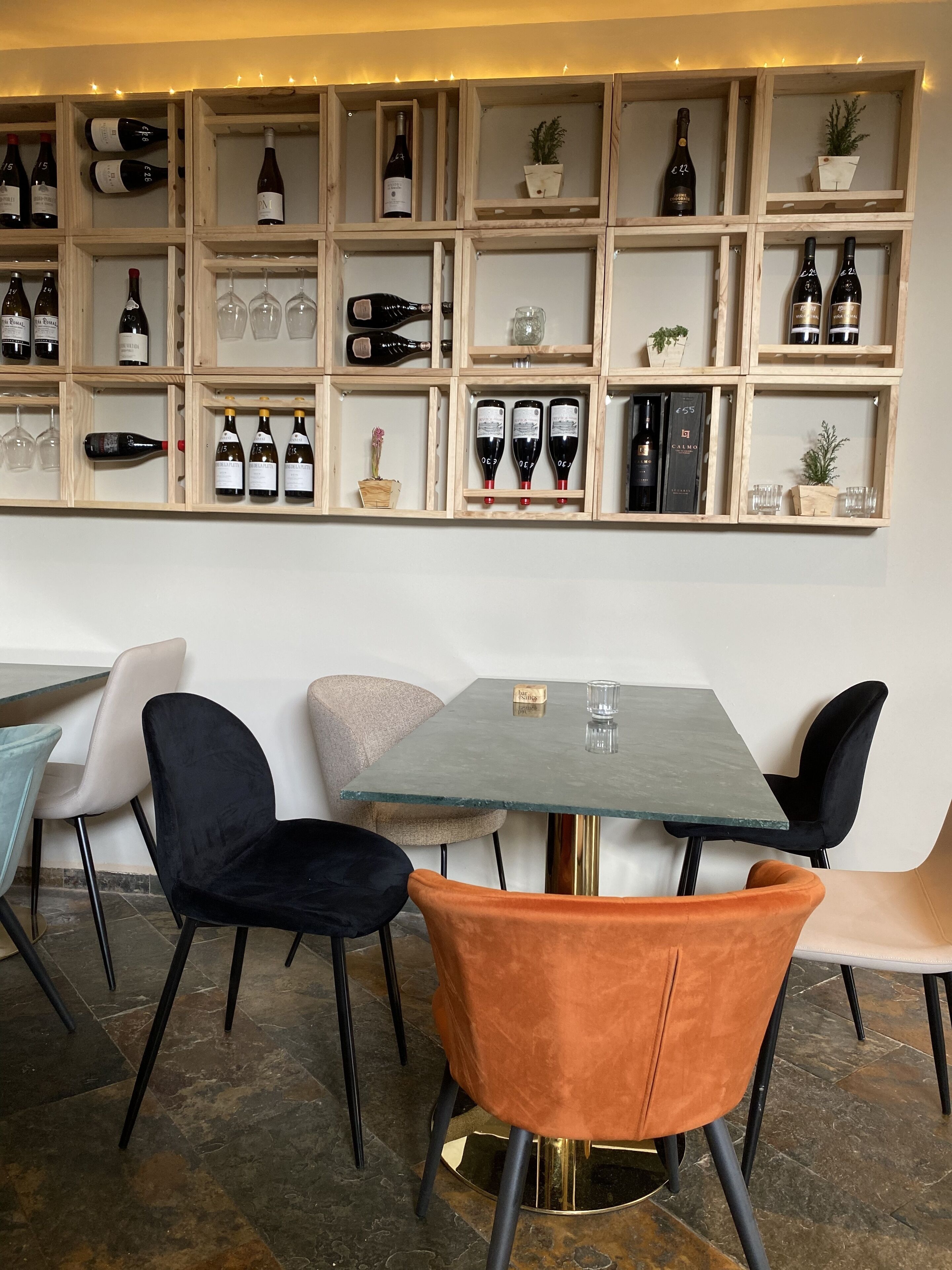 A restaurant interior with a wine display shelf, a table with chairs, and a bar area.