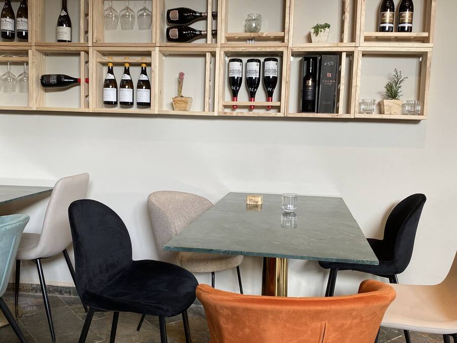 Interior de un restaurante con una estantería de vinos, una mesa con sillas y una zona de bar.
