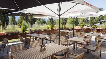Un espacio patio al aire libre con mesas y sillas de madera, cubierto por grandes sombrillas con la marca 'ESTRELLA DAMM'.