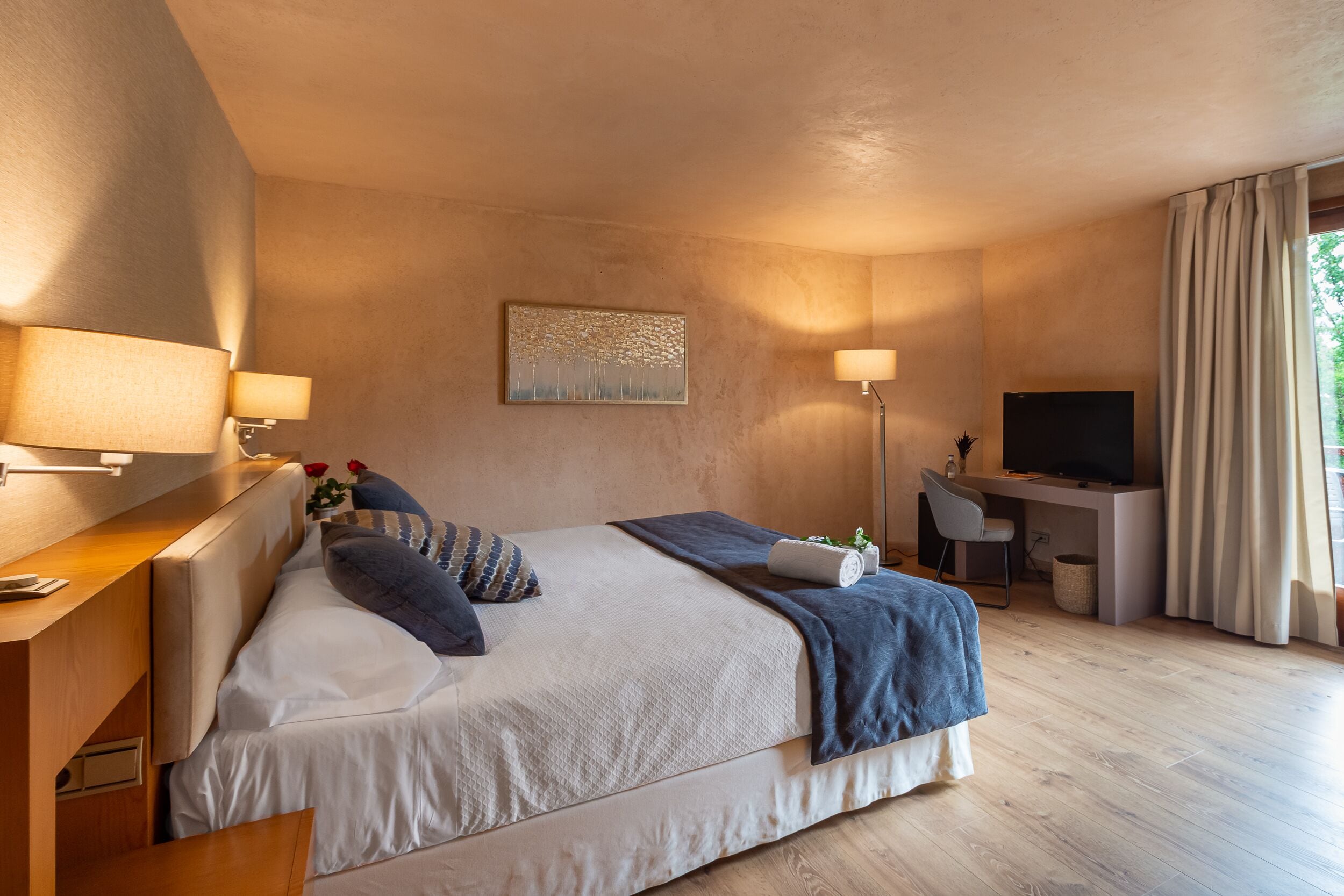 A modern hotel room with a large bed, a desk, a television, and a window with curtains.