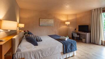 A modern hotel room with a large bed, a desk, a television, and a window with curtains.