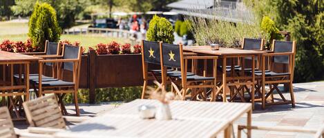 Outdoor wooden tables and chairs with black cushions and star designs, arranged on a stone patio.