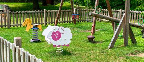 Un parque infantil con columpios, un sube y baja y un tobogán.