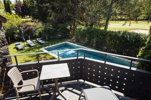 Zona junto a la piscina con una mesa y sillas, rodeada de exuberante vegetación y vistas a un campo de golf.