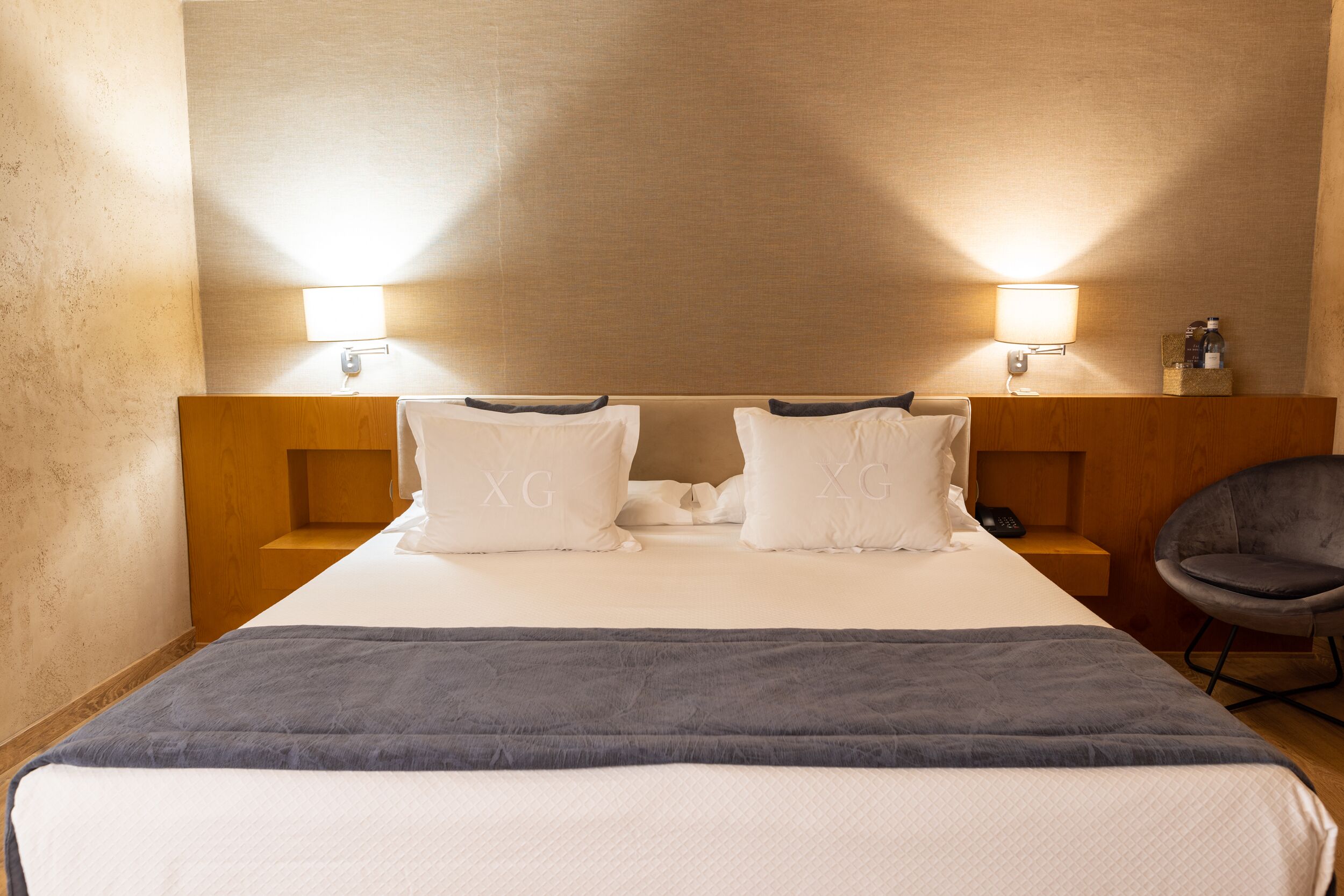 A hotel room with a large bed, two bedside tables, a chair, and two wall-mounted lamps.