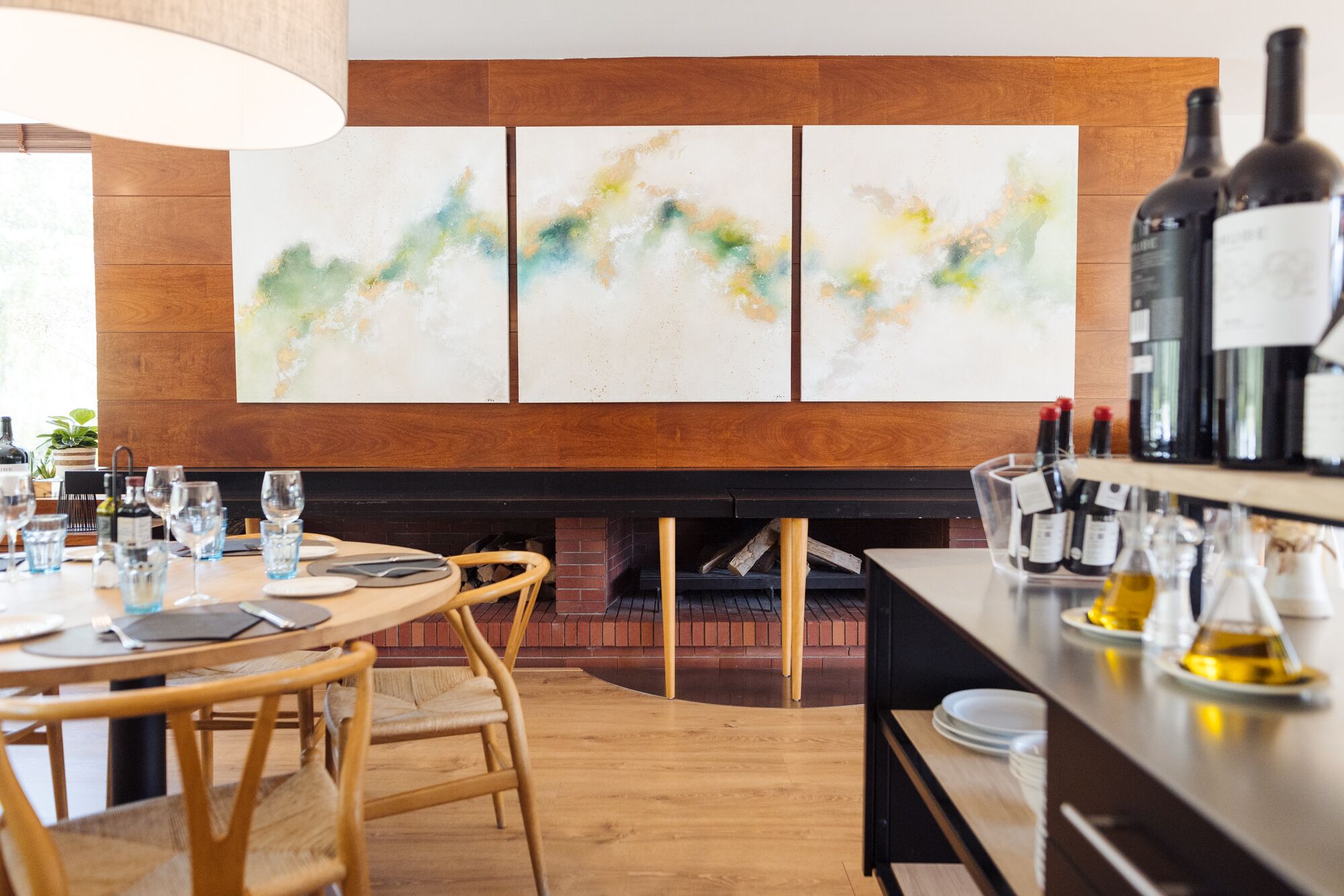 Un comedor moderno con chimenea de ladrillo, mobiliario de madera y arte abstracto en la pared.